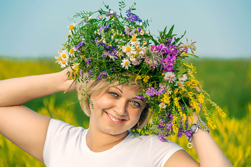 beautiful young woman walks in a field with a wreath of wild flowers.