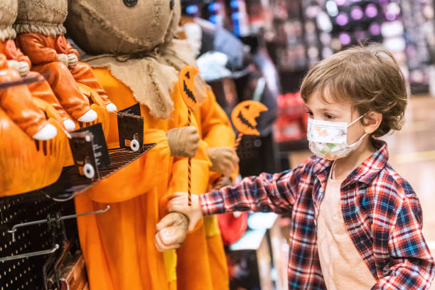 pensive little boy shopping for halloween decorations wearing a protective face mask - halloween color image horizontal side view imagens e fotografias de stock