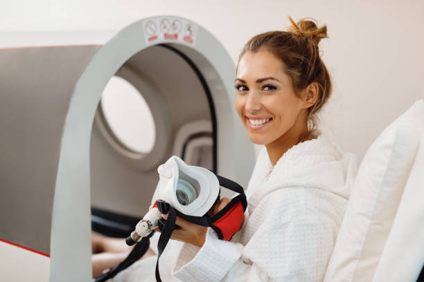 Happy woman having oxygen treatment in hyperbaric chamber at health spa. Young happy woman using oxygen mask during hyperbaric oxygen therapy at health spa. oxygen stock pictures, royalty-free photos & images