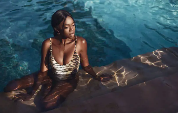 African beautiful young woman sitting by the pool in her bikini.