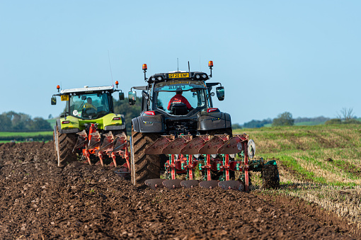 Castle Douglas, Scotland, UK - September 17, 2020: Two tractors ploughing a field on a farm in Dumfries and Galloway, south west Scotland. After ploughing the field will be sowed with wheat that will be harvested next summer and used to feed livestock during the winter months.