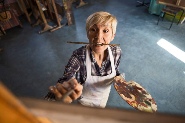 Aged woman in studio painting on canvas in workshop