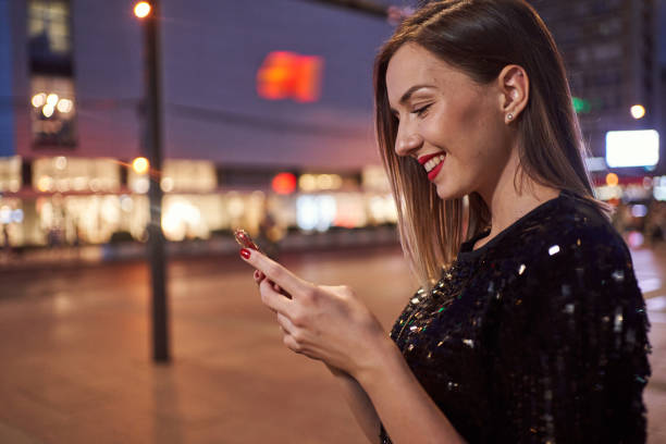 istock Cheerful young woman texting on a mobile phone outdoors at night 1279025878