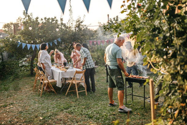 hombre mayor haciendo barbacoa para sus amigos durante la fiesta en el jardín - fiesta en el jardín fotografías e imágenes de stock