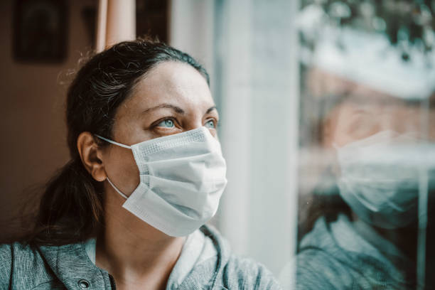 istock Woman with protective face mask looking trough the window during COVID-19 1279031295