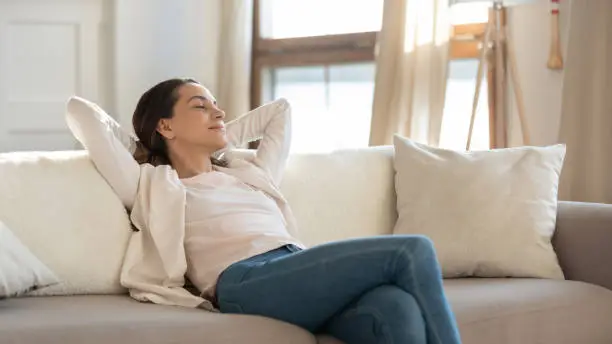 When all the work is done. Carefree confident millennial female or teenage girl student enjoying moments of tranquility and comfort relaxing on sofa indoors switching on air conditioner and humidifier