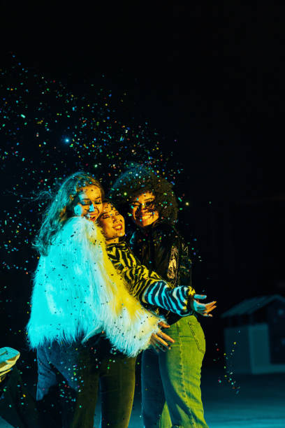 istock Three happy female friends embracing each other while standing under confetti at night 1279040742