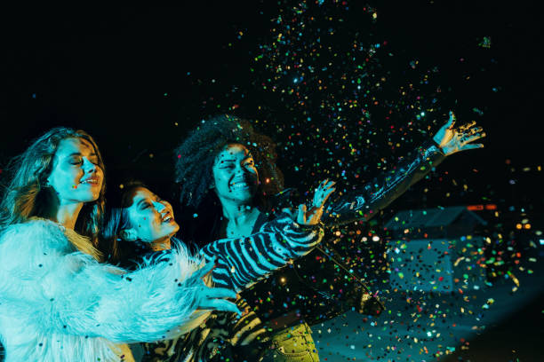 istock Three happy girls throwing confetti while standing on the roof under neon lights 1279040808