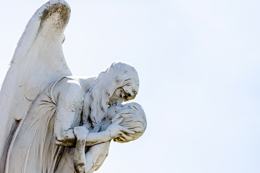 Old statue of angle kissing young boys in Waverley cemetery build in 1877 Sydney Australia, light blue sky background with copy space, horizontal composition
