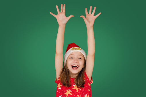 Happy Young Girl In Christmas Outfit Cheering With Hands In The Air On Deep Green Background With Copy Space