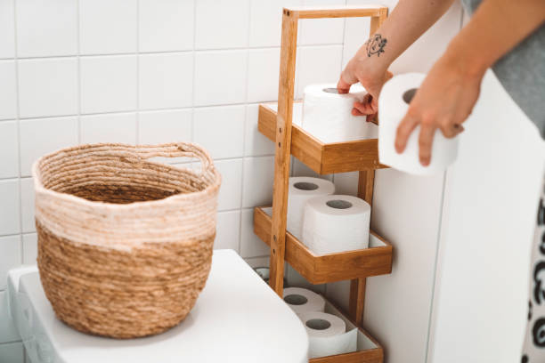Caucasian woman stocking up on toilet paper during pandemic crisis. Woman putting toiled paper rolls on to bamboo stand next to the toilet.