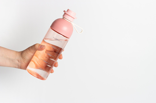 A female hand holds water bottle on a white background, copy space