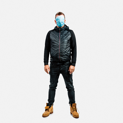 Full length of scared mature man protecting himself from pandemic crisis. Male is covering face with protective masks. He is standing against white background.