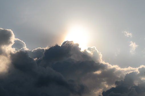 Concept of overcast, weather forecast, weather phenomenon, bright sunny day. In the image is a beautiful daytime phenomenon observed during overcast weather forecast. The clouds are covering the bright daytime sun and it appears that sun is peeping from behind the clouds. The clouds are huge, fluffy and might rain anytime, and since the clouds are transient and moving fast, it uncovers the sun in a while and it becomes a sunny day again. Formation of rainbow occurs during such kind of season.