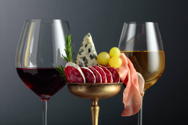 Wine, blue cheese, dry-cured sausage, grapes, and rosemary on a black background.