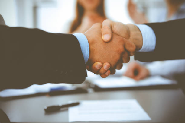 istock Business people shaking hands at meeting while theirs colleagues clapping and applauding. Group of unknown businessmen and women in modern white office. Success teamwork, partnership and handshake concept 1279101808