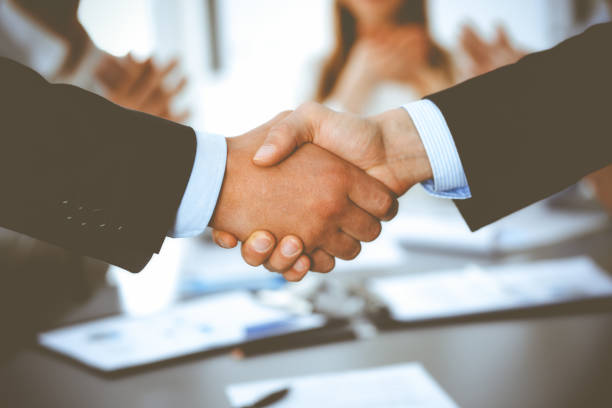 istock Business people shaking hands at meeting while theirs colleagues clapping and applauding. Group of unknown businessmen and women in modern white office. Success teamwork, partnership and handshake concept 1279101837