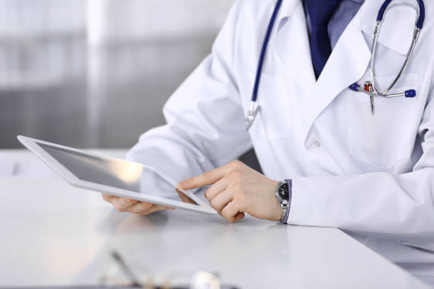 istock Unknown male doctor sitting and working with tablet computer in clinic at his working place, close-up. Young physician at work. Perfect medical service, medicine concept 1279103034