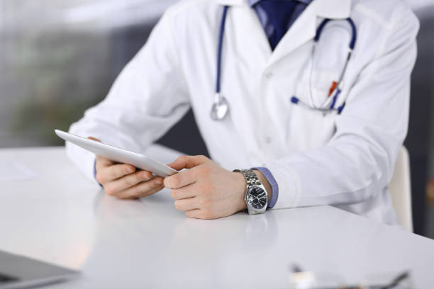 istock Unknown male doctor sitting and working with tablet computer in clinic at his working place, close-up. Young physician at work. Perfect medical service, medicine concept 1279103036