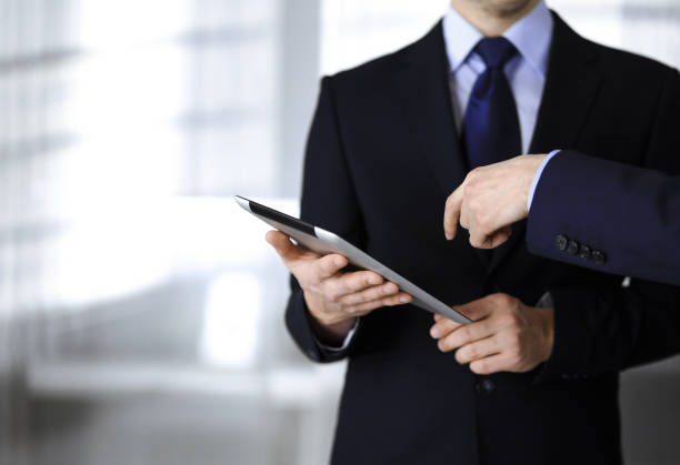istock Business people use a tablet computer for discussion of their new project, standing in a modern office. Unknown businessman or male entrepreneur with a colleague at workplace. Teamwork and partnership concept 1279103675