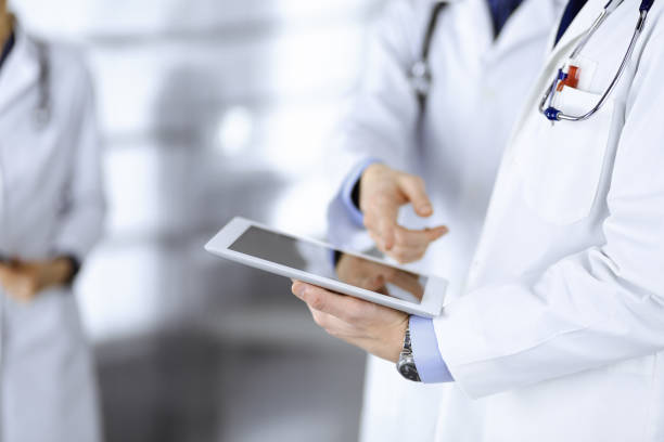 istock Group of unknown doctors use a computer tablet to check up some medical names records, while standing in a hospital office. Physicians ready to examine and help patients. Medical help, insurance in health care, best desease treatment and medicine concept 1279103698