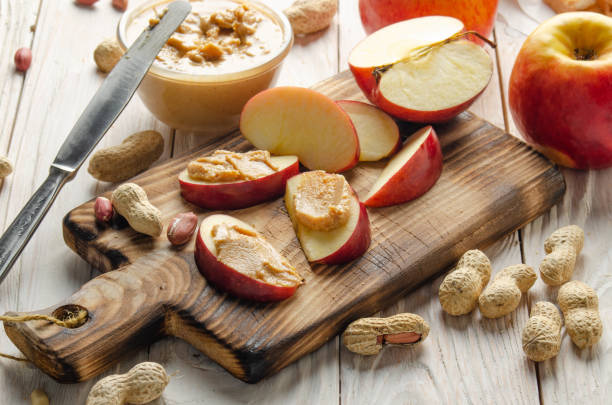 istock Cut board with apple slices with peanut butter on white wooden kitchen table 1279106823