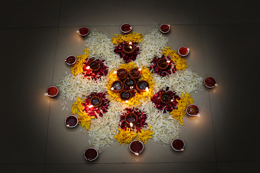 Beautiful Rangoli made by flower petals on Diwali festival and some of oil lamps burning on Diwali. Rangoli is an art form, originating in the Indian subcontinent, in which patterns are created on the floor or the ground using materials such as colored rice, dry flour, colored sand or flower petals.