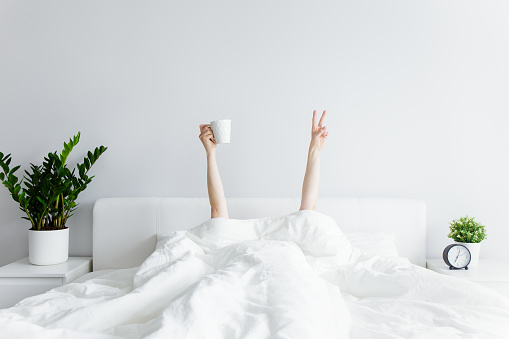 concepto de la mañana - manos femeninas con taza de café y signo de victoria que sobresale de la manta en casa u hotel photo