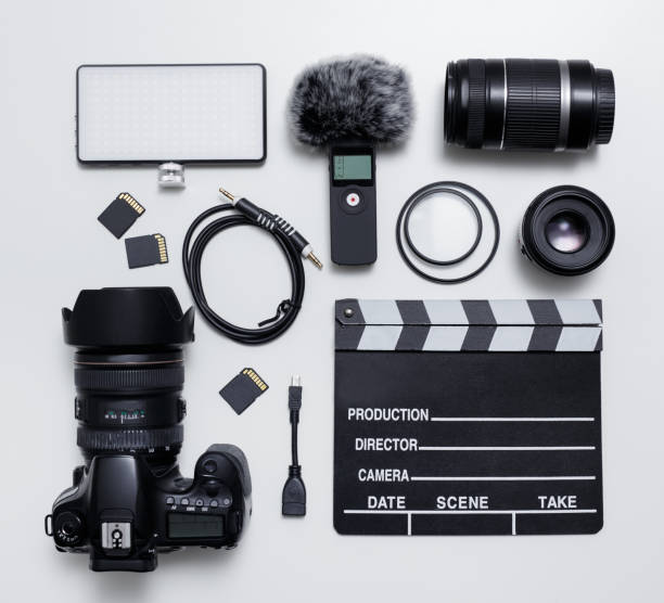 ビデオ撮影と写真機器 - 現代のデジタルカメラ、レンズ、フィルター、フロントガラス付きマイク、導かれた光、メモリカード、白いテーブルの上のクラッパーボードのトップビューフラッ�