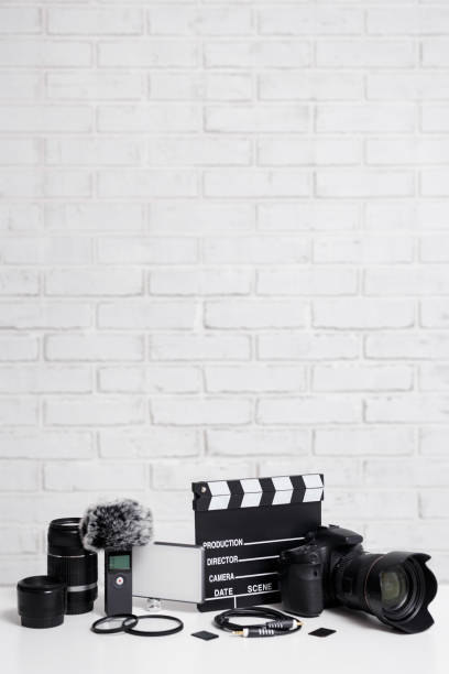 videography concept - modern dslr camera, lenses, microphone, led light, clapper board and other videography equipment over white brick wall background with copy space