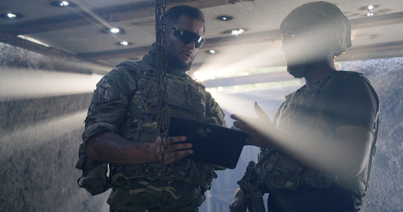 Low angle of bearded man talking and demonstrating data on tablet to commanding officer while discussing plan on base
