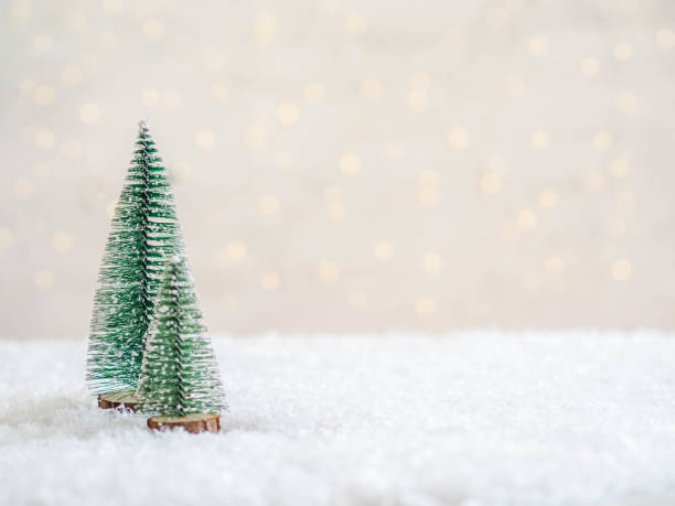 Christmas trees in the foreground in artificial snow and a blurred background with a glowing garland Christmas trees in the foreground in artificial snow and a blurred background with a glowing garland. Copy space. Front view. Minimal blurred background artificial flower stock pictures, royalty-free photos & images