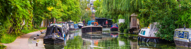 London barge piloting between narrow boats Regents Canal Camden panorama People living and working on the tranquil waters of the Regent’s Canal outside Camden Lock in the heart of Central London, UK. regents canal stock pictures, royalty-free photos & images