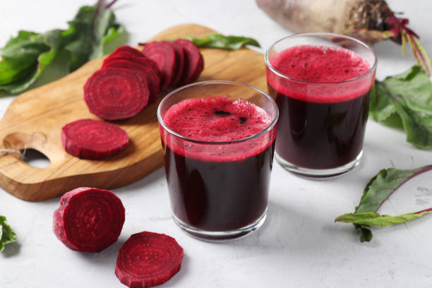 Two glass of fresh beetroot juice and chopped beet on wooden board on gray background. Closeup stock photo