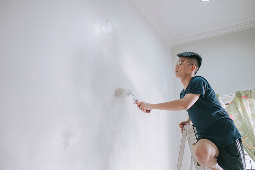 An asian chinese teenage boy painting his bedroom, apartment renovation during sunset