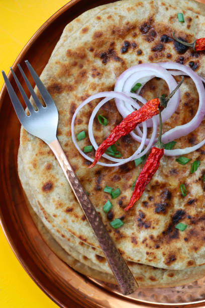 bild von metalltablett mit aloo paratha haufen mit chilischoten gekrönt, rote zwiebelringe und bestreuen von gehackten schnittlauch, herzhafte sendebrot gefüllt mit pürierten garam masala kartoffeln und metallgabel, gelber hintergrund, erhöhte ansicht - mashed potato food staple vertical color image stock-fotos und bilder