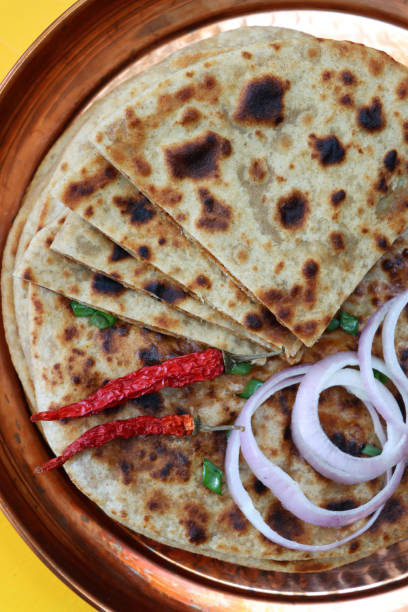 bild von metalltablett mit dreieckigen scheiben von aloo paratha haufen mit chilischoten, roten zwiebelringen und bestreuen von gehackten schnittlauch, herzhafte fladenbrot gefüllt mit pürierten garam masala kartoffeln und metallgabel, gelber hintergrund - mashed potato food staple vertical color image stock-fotos und bilder