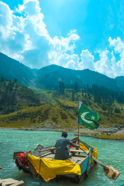 A guy sailing a boat in a lake at Kalam Valley Pakistan with Pakistan's flag on it.