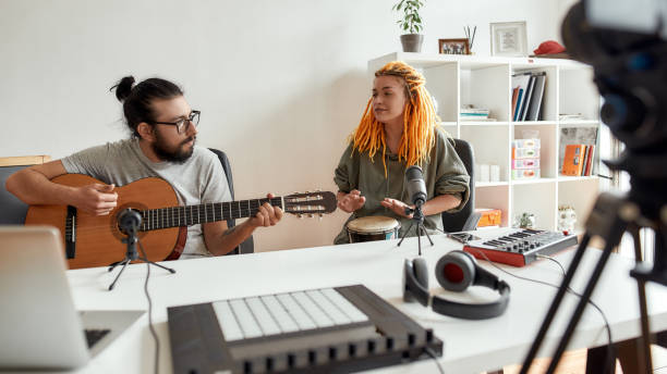 istock Inspiring others. Man playing guitar and woman singing, playing rhythm with djembe drum while recording video blog or vlog. Couple of musicians making music at home 1279140277