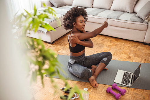 The morning stretch is important. Young black woman sitting on the floor at home stretching. Sport, fitness and healthy lifestyle concept - happy smiling young african american woman stretching arm at home