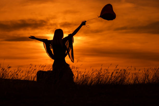 silhouette d’une femme s’asseyant sur la valise avec le ballon en forme de coeur - success determination idyllic carefree photos et images de collection