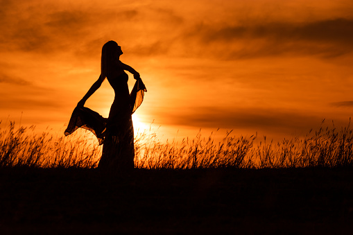 Happy woman dancing and holding scarf while enjoys spending time at sunset.