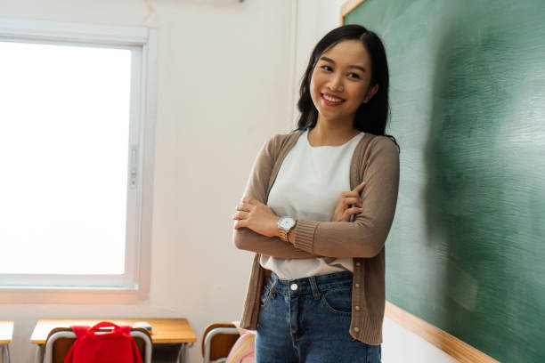 joven profesora asiática sonriendo por pizarra en el aula de la escuela - 20s attractive female beautiful people blackboard fotografías e imágenes de stock