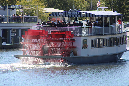 Paddlewheel Riverboat in the beautiful little town of Saugatuck in Michigan, USA. It's a cooler day and people are dressed warmly and standing on the deck overlooking the paddlewheels.