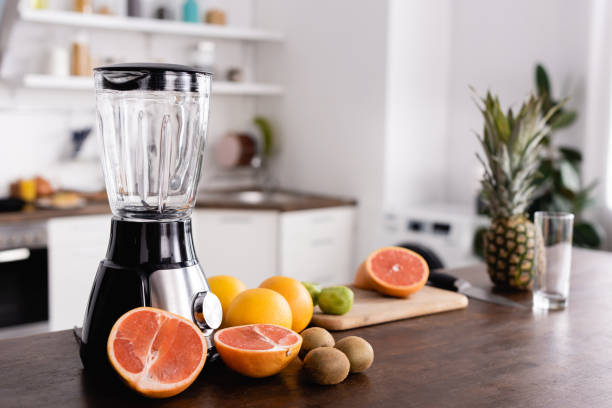 enfoque selectivo de frutas maduras cerca de la licuadora en la mesa de la cocina - blender fotografías e imágenes de stock