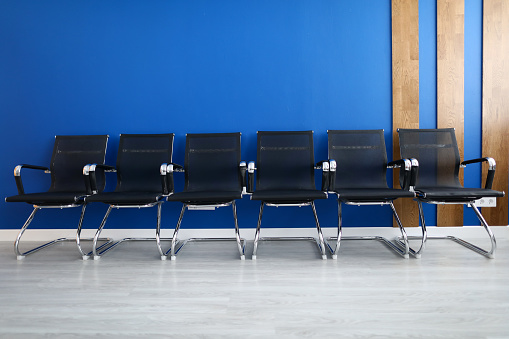 Black chairs on row against blue wall modern office closeup background. Business seminar concept
