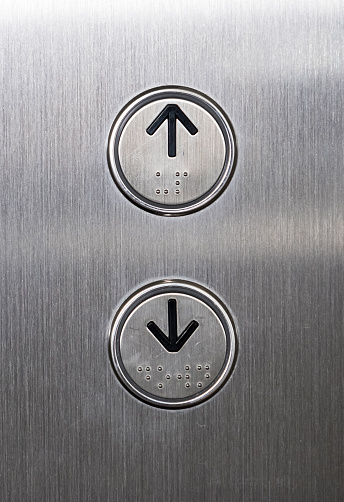 Arrow symbol with the braille on the push button of the metal panel in the passenger elevator,office building in the urban area.