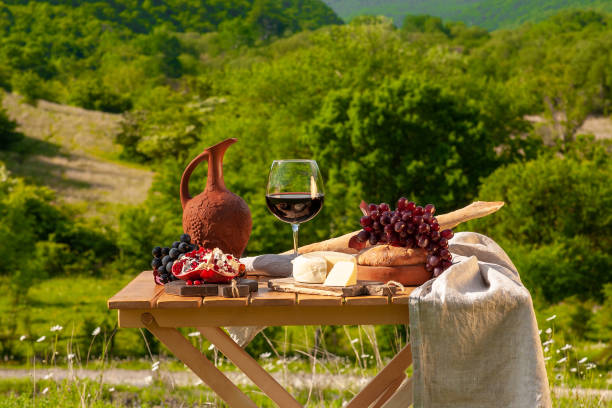 Outdoor picnics in the mountains. Outdoor picnics in the mountains. A picnic table set with red wine, cheese, fruits, grapes and bread stands in a meadow in green grass. The concept of secluded outdoor recreation. georgian style stock pictures, royalty-free photos & images