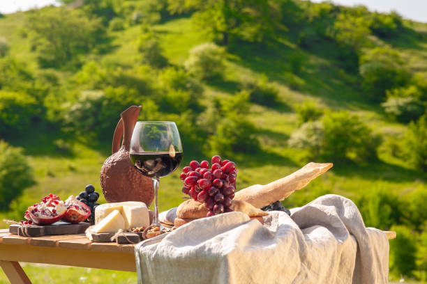 Outdoor picnics in the mountains. A picnic table set with red wine, cheese, fruits, grapes and bread stands in a meadow in green grass. The concept of secluded outdoor recreation.