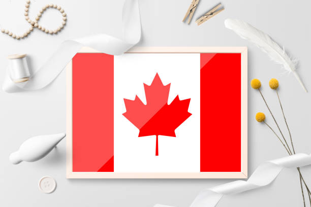 istock Canada flag in wooden frame on white creative background. White theme, feather, daisy, button, ribbon objects. 1279164813
